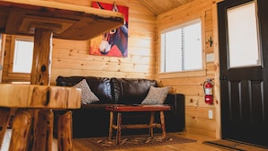 A wooden interior with a ceiling fan, a black leather couch, and a dining table. - The Big Texan - Cabins & Wagons  (Amarillo)