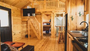 A wooden cabin interior with a staircase, a kitchen area, and a living space with a couch and a TV. - The Big Texan - Cabins & Wagons  (Amarillo)