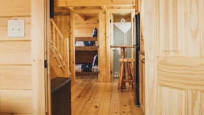 A wooden interior with a staircase leading to a loft bedroom, a small kitchen area, and a wooden door. - The Big Texan - Cabins & Wagons  (Amarillo)