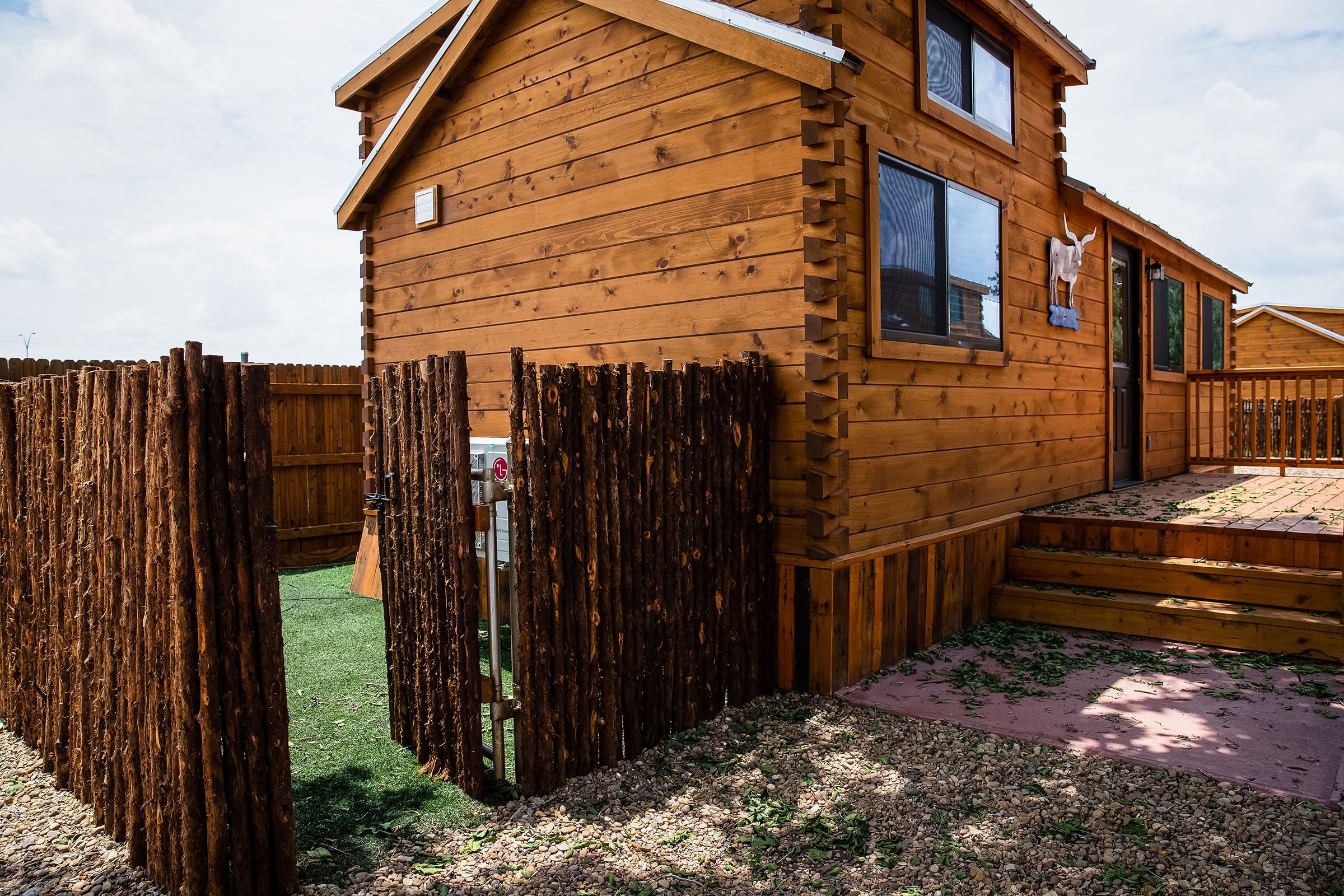 A wooden cabin with a fenced yard, a small porch, and a window with a decorative item.