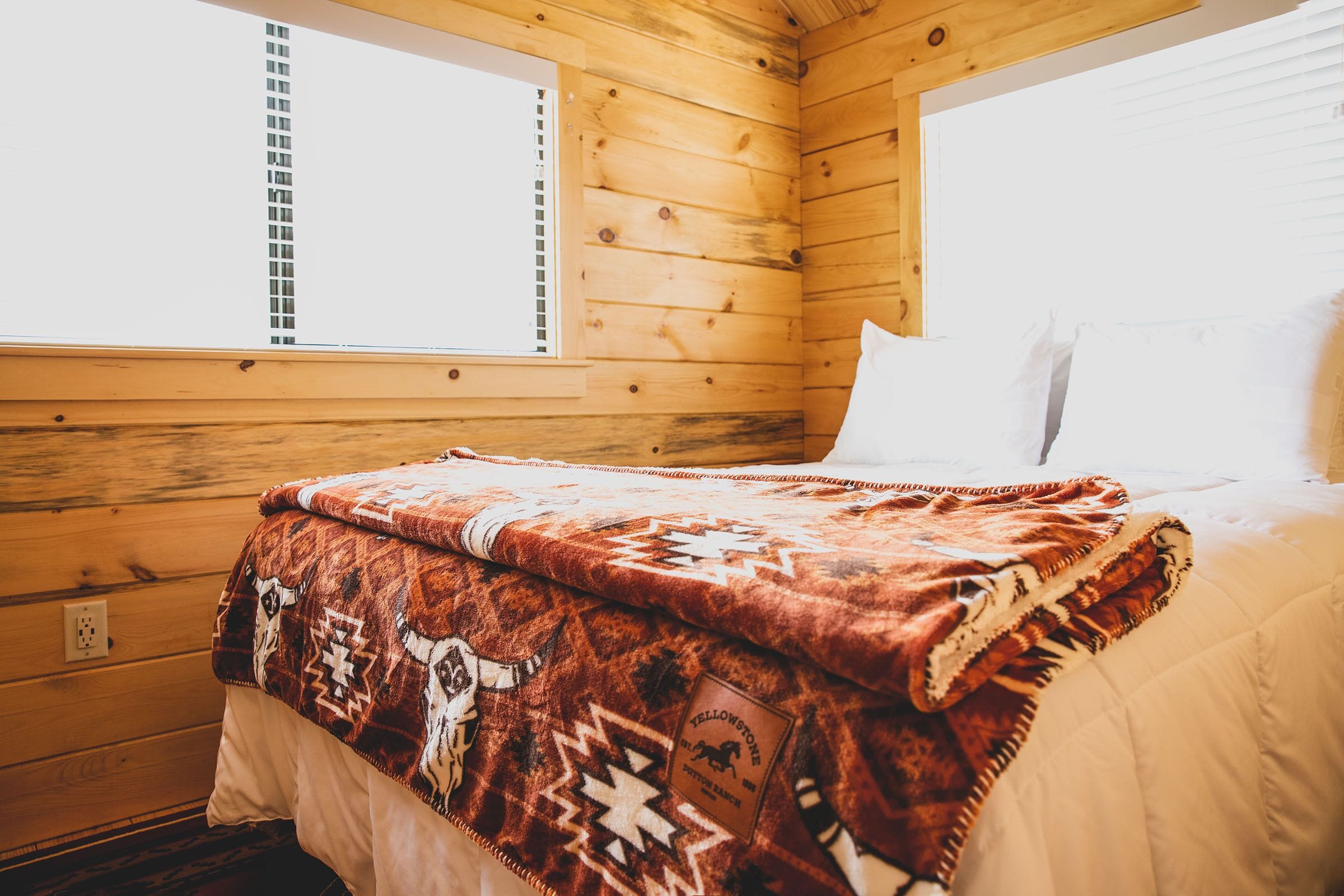 A wooden cabin room with a bed, a window, and a wall socket.