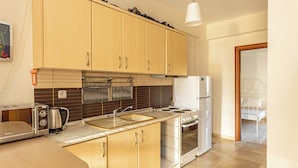 A kitchen with wooden cabinets, a stove, a sink, and a toaster. - Nano's Vacation In Nea Skioni  (Kassandra)