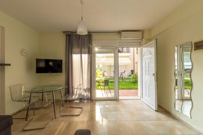 Uma sala de estar moderna com mesa de vidro, cadeiras, televisão de tela plana e porta de correr de vidro que dá para um pátio externo.