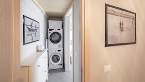 Ein Waschraum mit übereinander gestapelten Waschmaschinen und Trocknern, einem weißen Schrank und zwei gerahmten Bildern an der Wand.