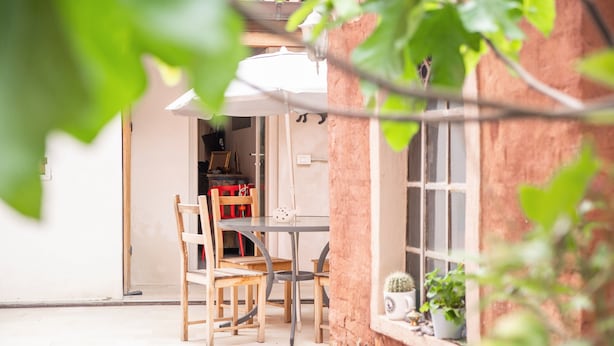 Ein rustikaler Essbereich im Freien mit Tisch und Stühlen, ein Fenster mit Blick und ein Blumentopf auf der Fensterbank.
