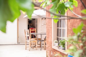 Un área de comedor al aire libre de estilo rústico, con una mesa y sillas, una ventana con vistas y una planta en maceta en el alféizar.