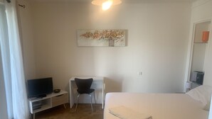 Hotellihuone, jossa on sänky, työpöytä, tuoli, televisio ja taulu seinällä.