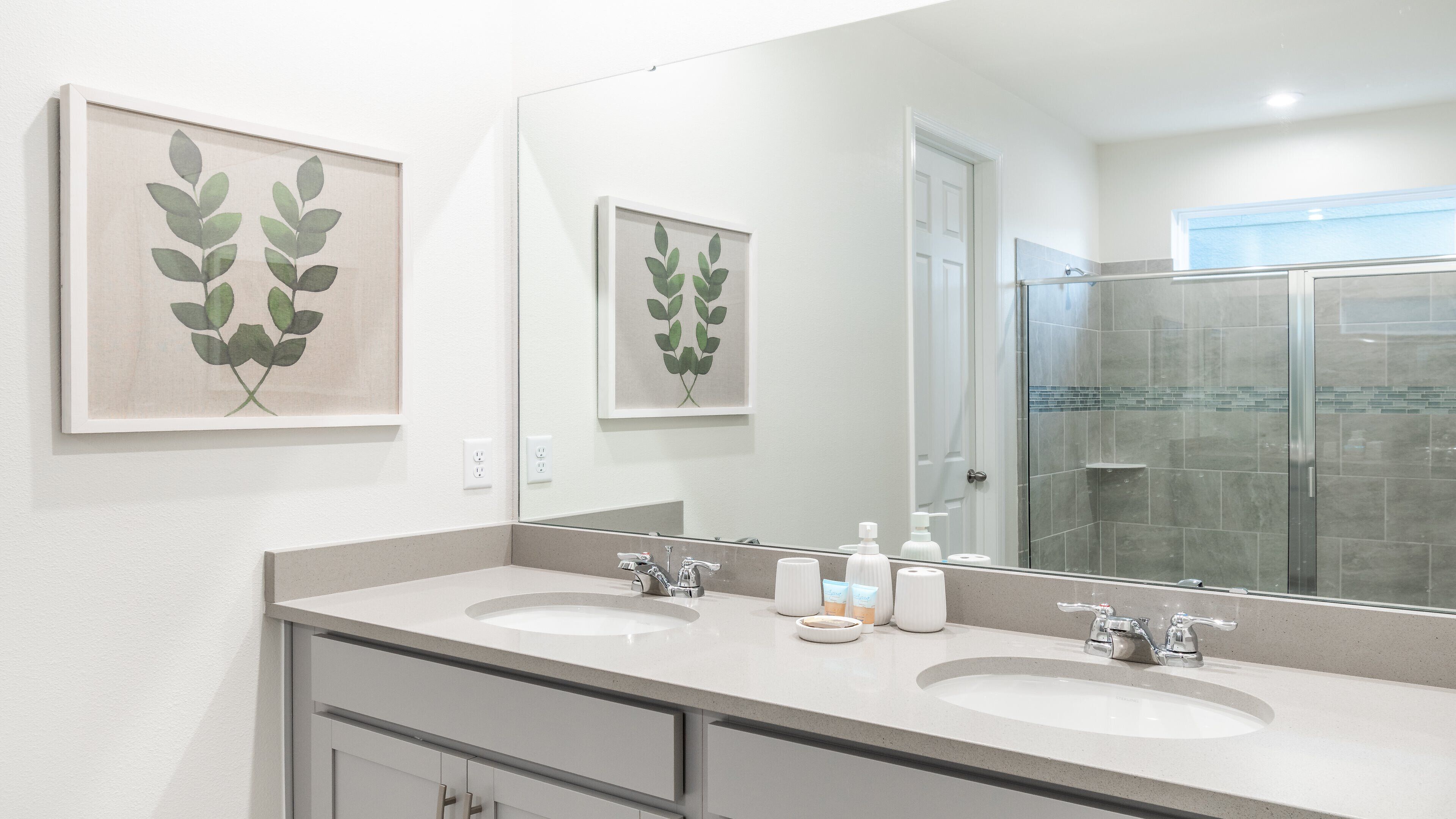 A bathroom with two sinks, a large mirror, and framed leaf artwork on the wall.