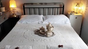 Una cama bien hecha con un cubrelecho blanco, una bandeja de té y una lámpara de noche.