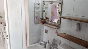 Un baño con un lavamanos blanco, un espejo con marco floral y un estante de madera.