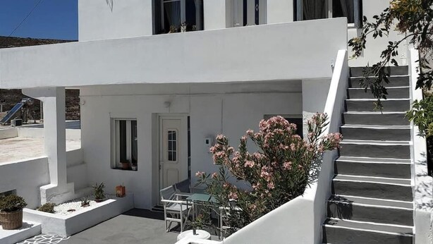 Un edificio blanco con un espacio exterior cubierto, una escalera y un pequeño jardín con flores rosas.