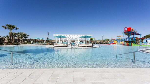 A large outdoor swimming pool with lounge chairs and umbrellas, a water play area, and a covered seating area.