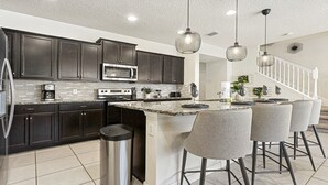 A modern kitchen with dark cabinets, stainless steel appliances, a granite countertop, and a bar area with bar stools.