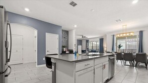A modern kitchen with a central island, white cabinetry, and a dining area with a table and chairs. - Last Minute Disney! Private Pool, Hot Tub, Game Room & Themed Bedrooms. Book Now! #57281 (Orlando)