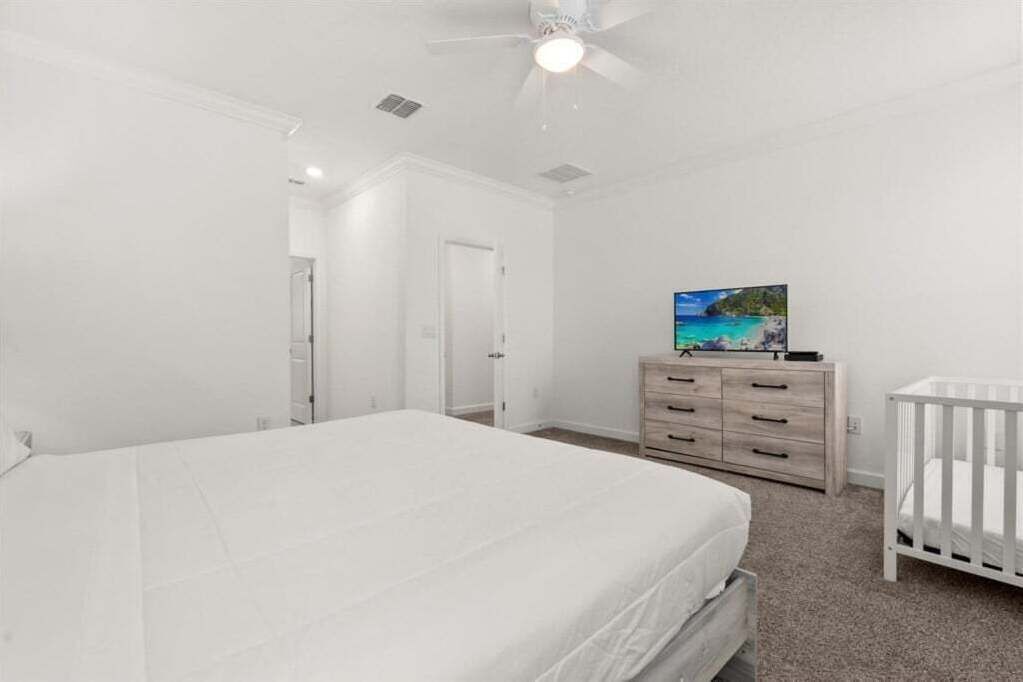 A bedroom with a bed, a dresser, a crib, and a ceiling fan.