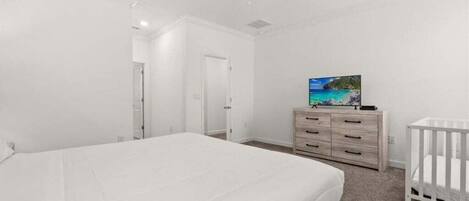 A bedroom with a bed, a dresser, a crib, and a ceiling fan.