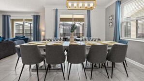 A dining area with a rectangular table set for six, surrounded by grey chairs, a chandelier, and a view through a glass door to a balcony. - Last Minute Disney! Private Pool, Hot Tub, Game Room & Themed Bedrooms. Book Now! #57281 (Orlando)