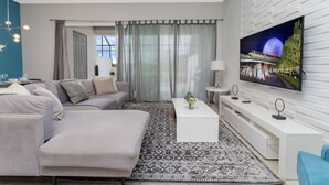 Una sala moderna con un sofá seccional gris, una mesa de centro blanca y un televisor de pantalla plana grande montado en una pared blanca.