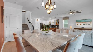 Une cuisine moderne avec des meubles blancs, un îlot central agrémenté de plantes et un coin repas avec une table et des chaises en marbre.
