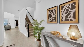 Un intérieur moderne avec un escalier, une plante en pot et deux œuvres d’art abstraites accrochées au mur.