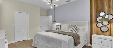Un dormitorio con una cama blanca, un panel de pared de madera, un aplique de techo y una mesita de noche.