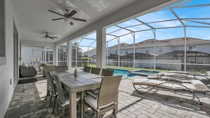 Une terrasse couverte avec une piscine, des meubles en osier et une vue sur les maisons au loin.