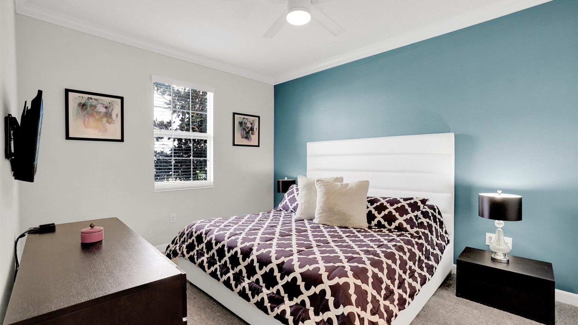 Un dormitorio con cama, escritorio, silla, mesita de noche y lámpara.