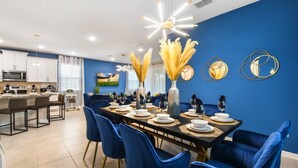 Ein moderner Essbereich mit einem langen Tisch, gedeckt für sechs Personen, blauen Stühlen und dekorativen Vasen mit Pampasgras.