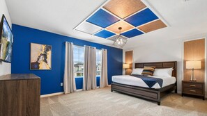 Un dormitorio moderno con una pared azul de acento, una cama grande con cabecera de madera, un techo con diseños geométricos y vistas al exterior a través de la ventana.