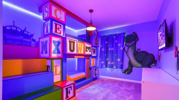 Una habitación con bloques de letras de colores, una decoración de dinosaurio y una alfombra morada.