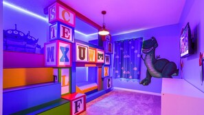 Une pièce décorée de blocs de construction colorés représentant l’alphabet, d’une décoration sur le thème des dinosaures et d’un tapis violet.