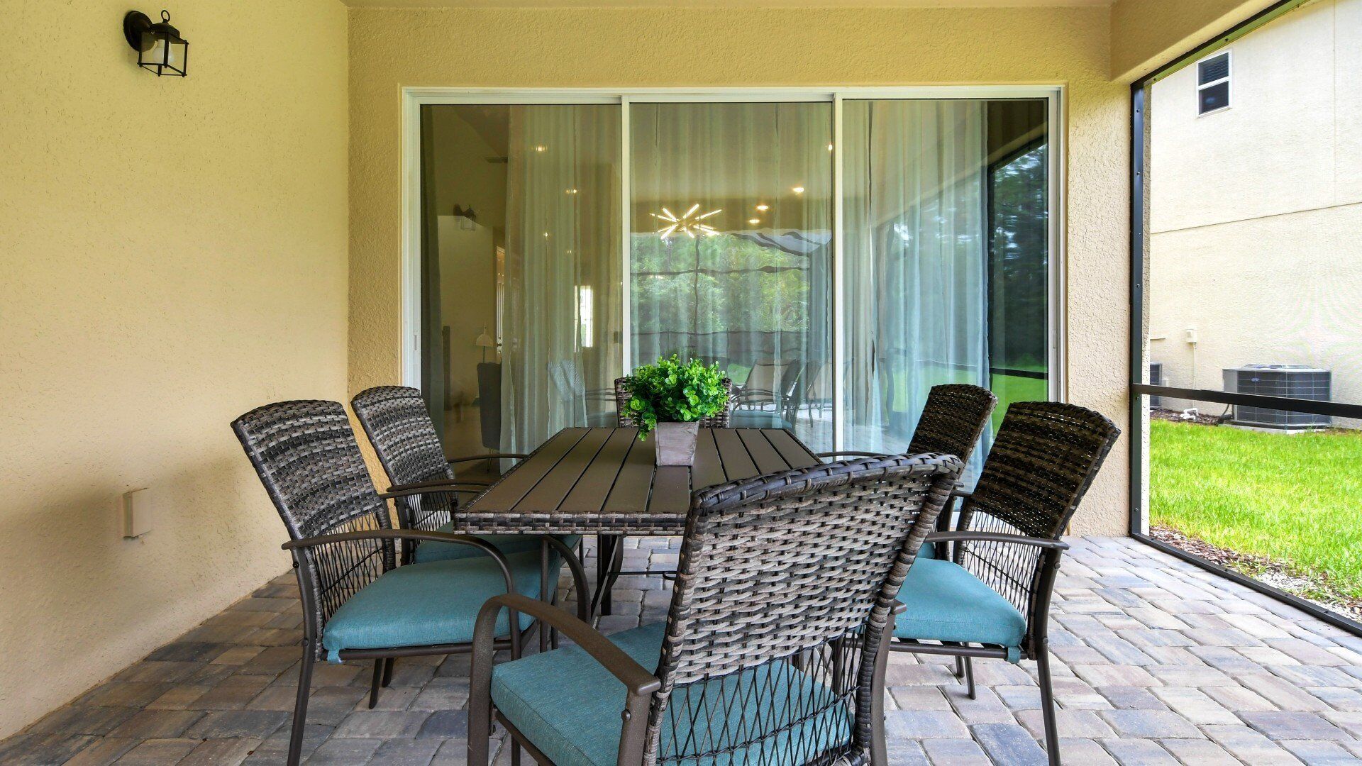 A patio with a table and chairs, a potted plant, and a sliding glass door leading to a grassy area.