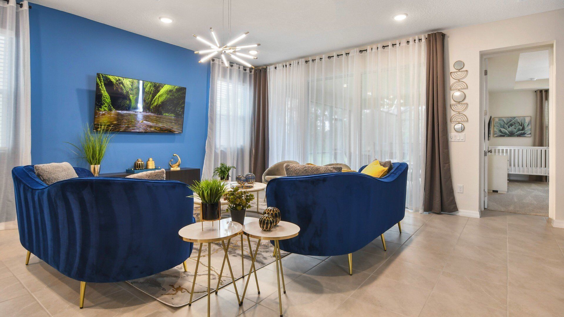 A modern living room with two blue armchairs, a round coffee table, and a large TV on a blue wall.