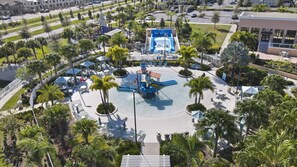 Vue aérienne d’un parc aquatique avec une grande toboggan aquatique au centre, entouré de palmiers et de zones aménagées avec des sièges en plein air.