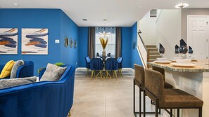 Una sala moderna con un sofá azul, un comedor con mesa y sillas, y una cocina con mostrador y sillas.