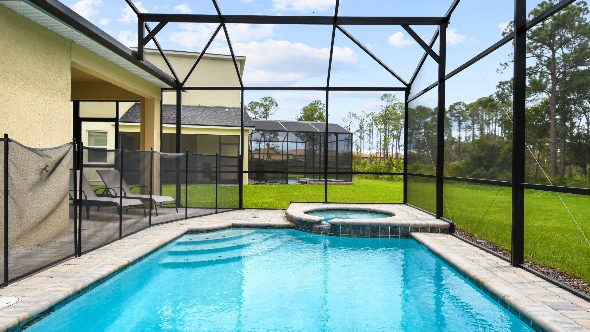 A swimming pool with a hot tub, surrounded by a covered patio area with a view of a house and trees.