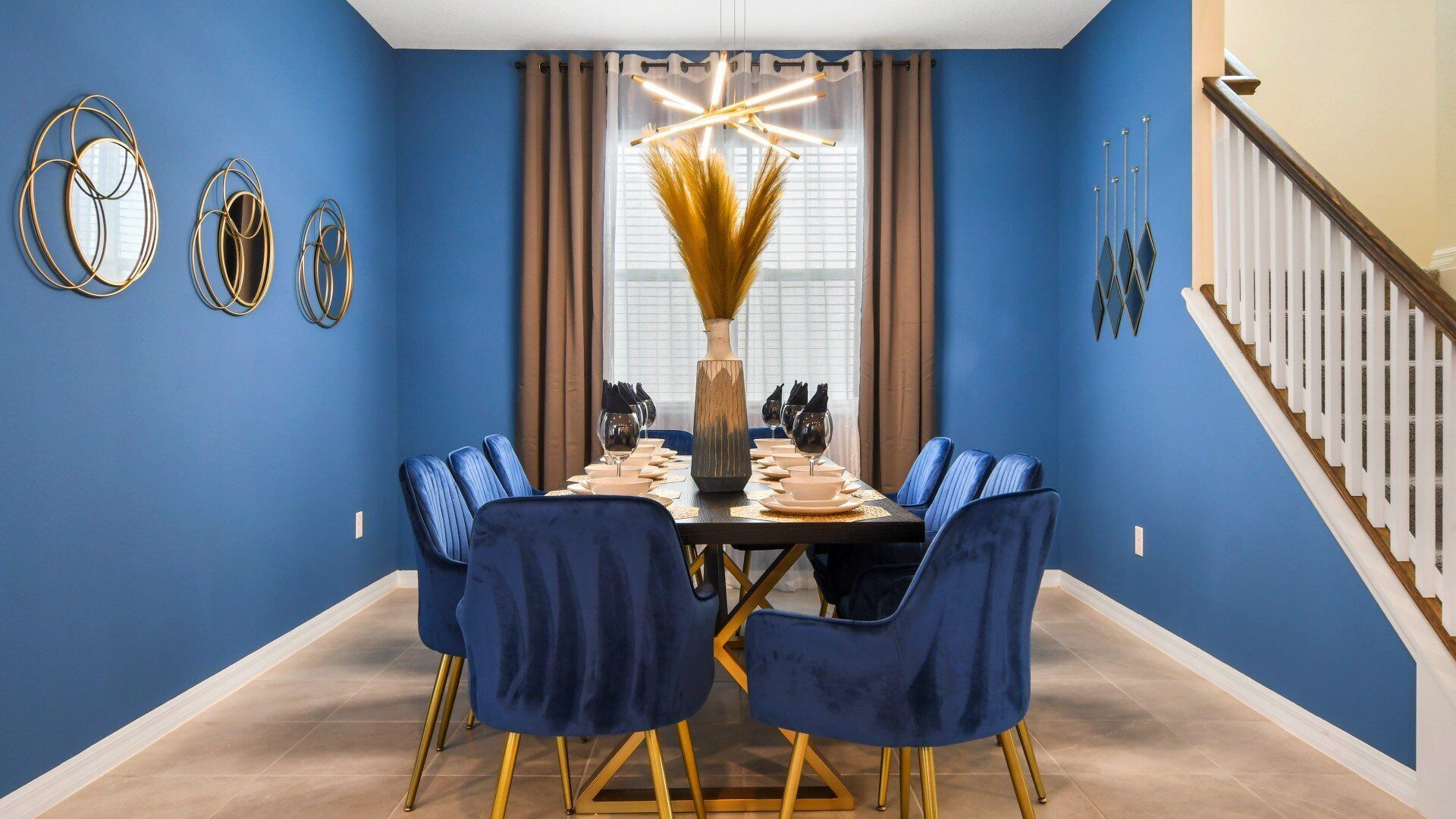 A dining room with a blue wall, a chandelier, and a staircase.