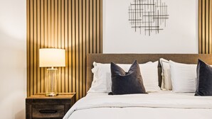 A neatly made bed with white linens and dark pillows, a bedside lamp, and a wall with vertical wooden slats. - Last Minute Disney! Private Pool, Hot Tub & Themed Bedrooms. Book Now! #79721 (Orlando)