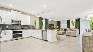 A modern kitchen with white cabinets, a microwave, and a dishwasher. There is a dining area with a sofa and a coffee table. - Last Minute Disney! Private Pool, Hot Tub & Themed Bedrooms. Book Now! #79721 (Orlando)