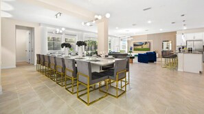 Una cocina amplia con una isla central, un comedor con una mesa larga y sillas, y una sala de estar con un sofá y televisor.