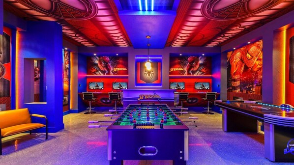 Una habitación con mesa de fútbolín, dos zonas de bar y un gran mural con temática de Spider-Man en la pared.