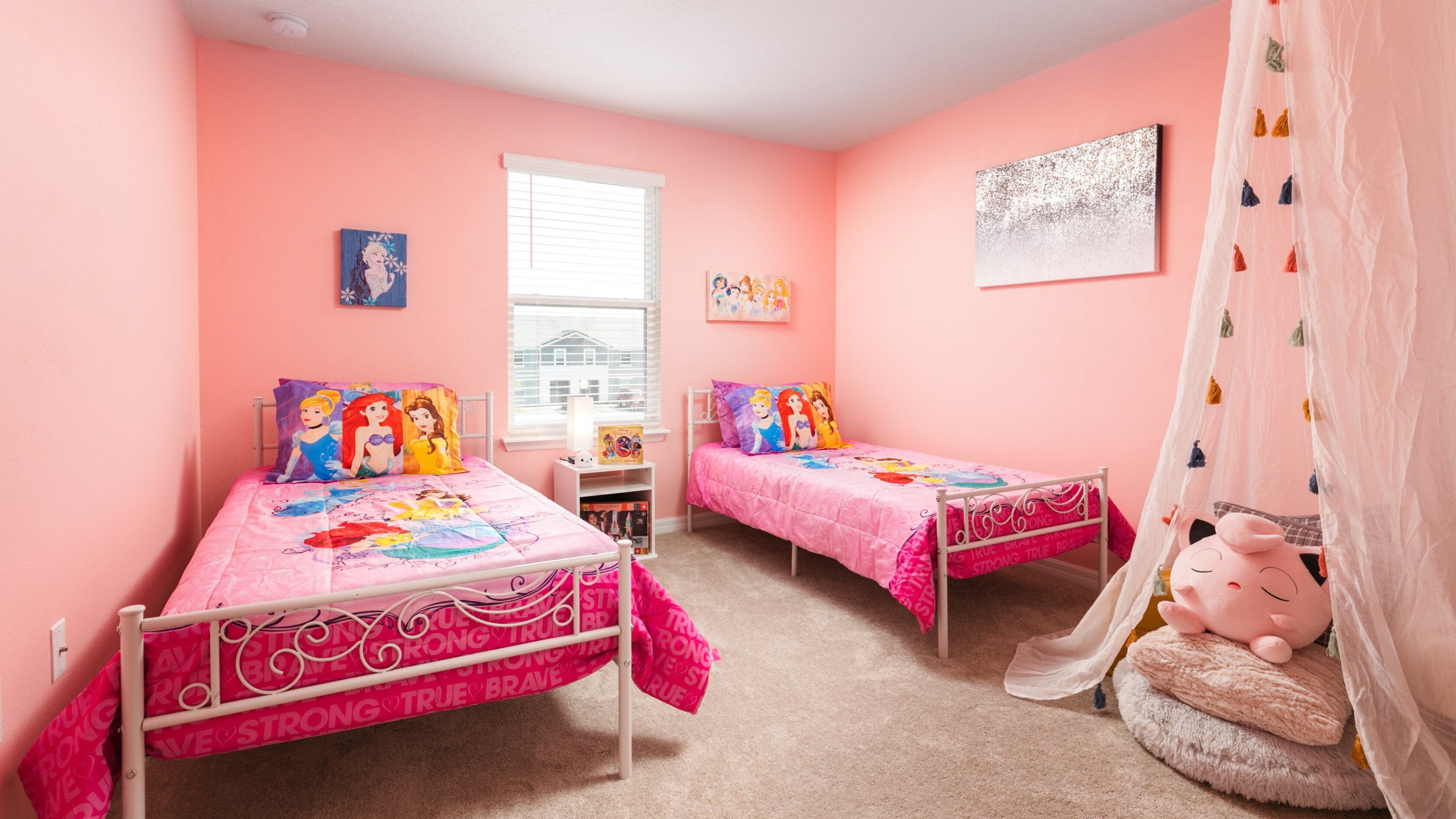 Dormitorio rosa con dos camas, cada una decorada con ropa de cama con temática de princesas Disney.
