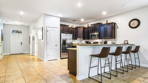 Una cocina moderna con alacenas de madera oscura, un refrigerador de acero inoxidable, un microondas y un lavamanos. Hay cuatro taburetes en la isla.