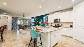 Una cocina moderna con armarios blancos, una isla central y un comedor con cortina estampada.
