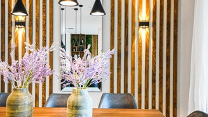 Un comedor con una mesa de madera, dos jarrones con flores moradas y lámparas colgantes negras.