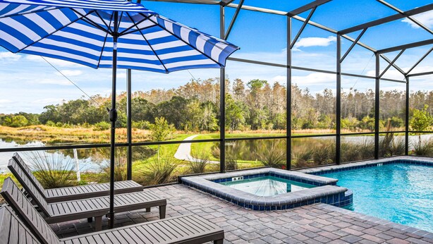 A pool area with a view of a lake and forest, surrounded by a glass enclosure. - Last Minute Disney! Private Pool, Hot Tub, Game Room & Themed Bedrooms. Book Now! #81845 (Orlando)