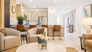 A modern living room with a marble coffee table, beige sofas, and a kitchen in the background. - Last Minute Disney! Private Pool, Hot Tub, Game Room & Themed Bedrooms. Book Now! #81845 (Orlando)