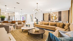 A spacious living room with a large beige sofa, a coffee table, and a dining area with chairs. - Last Minute Disney! Private Pool, Hot Tub, Game Room & Themed Bedrooms. Book Now! #81845 (Orlando)