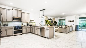 A modern kitchen with a central island, built-in appliances, and a dining area with a sofa. - Last Minute Disney! Private Pool, Hot Tub, Game Room & Themed Bedrooms. Book Now! #81847 (Orlando)