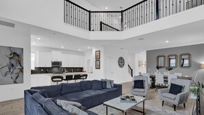 Amplia sala de estar con un sofá seccional azul grande, una mesa de centro y un comedor con sillas blancas y una mesa.